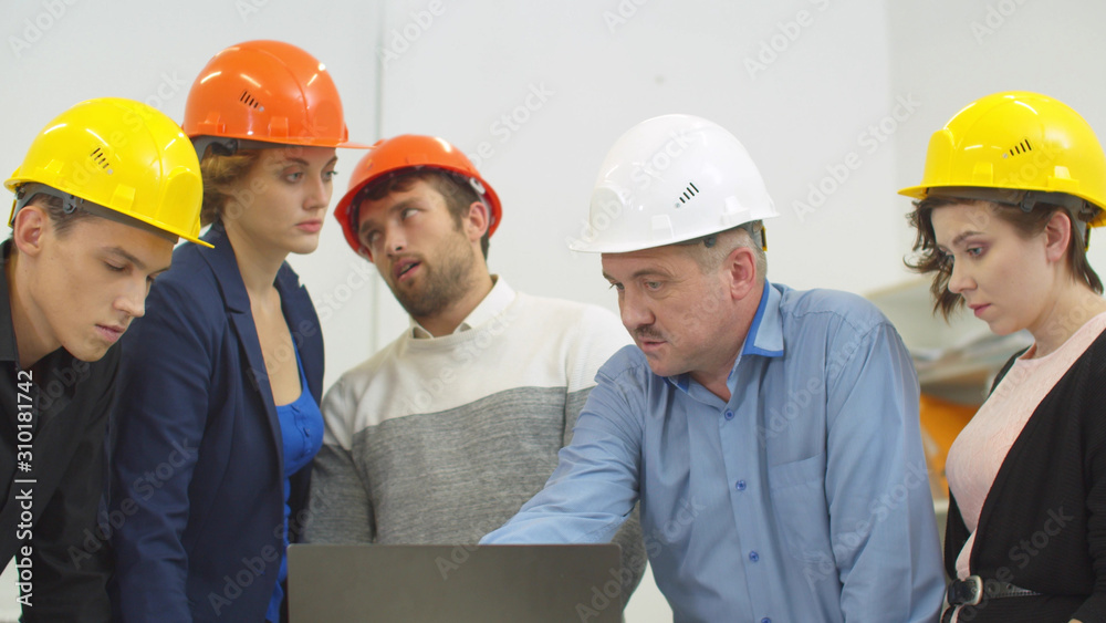 Man in helmet explains something to his colleagues with laptop Man in helmet explains something to his colleagues with laptop