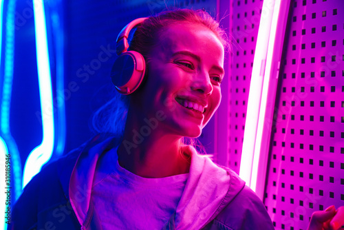 Image of woman listening to music with headphones over neon illumination photo