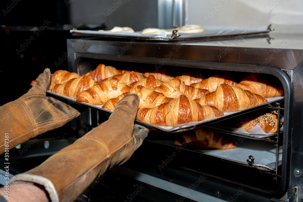 Taking out of the oven, freshly baked croissants in a bakery in Madrid, Spain