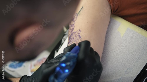 Close up footage of tattoo artist demonstrates the process of getting colour tattoo. Animalconcept. Modern tattoo parlor. Top view of tattoo artist and his female client in a beauty salon photo