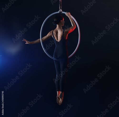 Young woman performing acrobatic element on aerial ring against dark background © New Africa