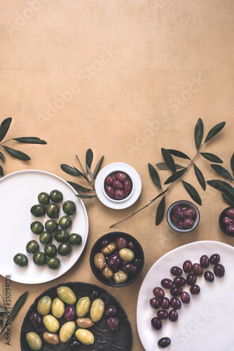 Flat-lay of various kinds of Mediterranean pickled olives for the appetizer in plates and bowls and olive tree branches on pastel color  background, top view, copy space photo