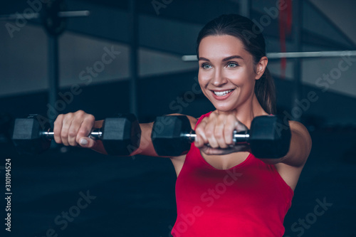 Slim fit muscular brunette woman exercise in gym, lifting weights and doing pilates. Picture with dark evening mood and film color grading.