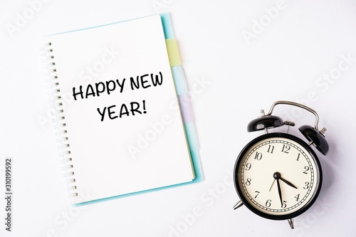 Happy New Year wordings on a notebook with a black alarm clock