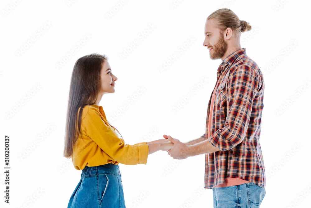 side view of young couple in casual outfit holding hands and looking at each other isolated on white side view of young couple in casual outfit holding hands and looking at each other isolated on white
