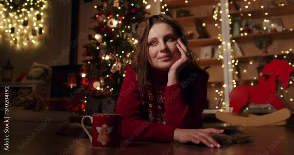 A thoughtful beautiful girl lies in a beautiful cozy decorated country house near the Christmas tree and emotionally thinks, doubts and makes a wish. Christmas idyll A thoughtful beautiful girl lies in a beautiful cozy decorated country house near the Christmas tree and emotionally thinks, doubts and makes a wish. Christmas idyll
