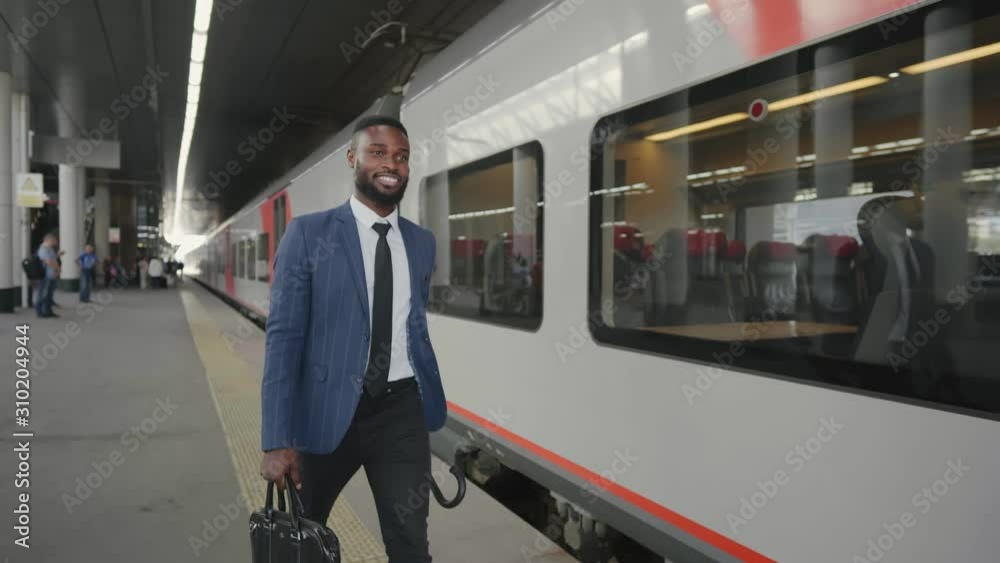 Cheerful businessman with briefcase and umbrella walking along train platform going to work by train