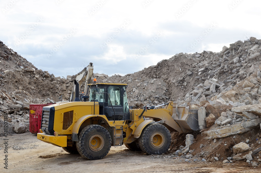 Salvaging and recycling building and construction materials. Industrial waste treatment plant. Excavator and a front-end loader work at landfill with concrete demolition waste. Re-use concrete