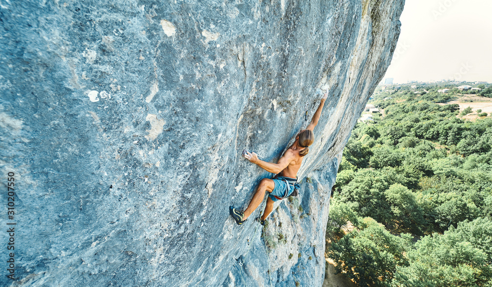 top view strong muscular man rock climber with naked torso dynamically climbing on a vertical cliff, making hard wide move and gripping hold. top view strong muscular man rock climber with naked torso dynamically climbing on a vertical cliff, making hard wide move and gripping hold.