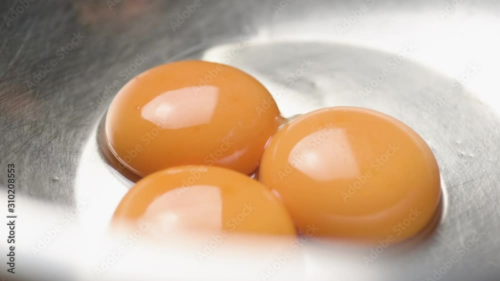 Close up of an egg yolk sliding into two other egg yolks inside a metal