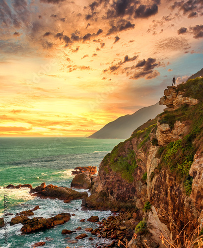 A man stands on a cliff by ocean in sunset