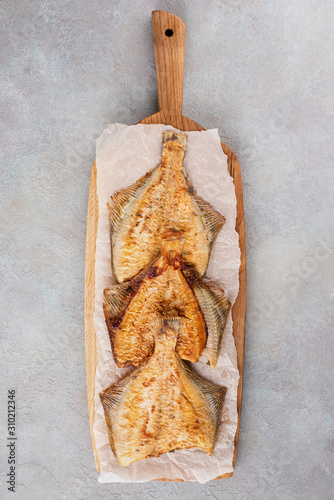 Grilled flounder on a serving oak board on a light background. Flat lay.