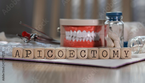 Word APICOECTOMY composed of wooden dices. Pills, documents, pen, human jaw model in the background. photo