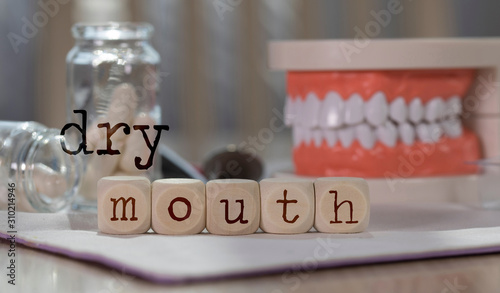 Words DRY MOUTH composed of wooden dices. Pills, documents, pen, human jaw model in the background. photo