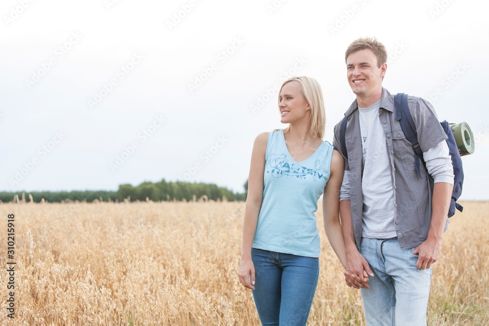 Young hiking couple holding hands while standing on field