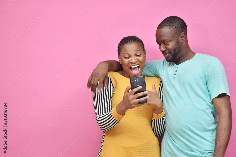 Obraz premium two young african friends, boy and girl, looking excited while viewing something on their smartphone together
