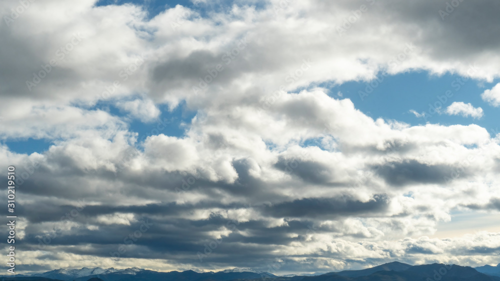 Fototapeta premium Colorful evening clouds on a bright blue sky above the peaks of the mountains in the distance. Beautiful landscape background