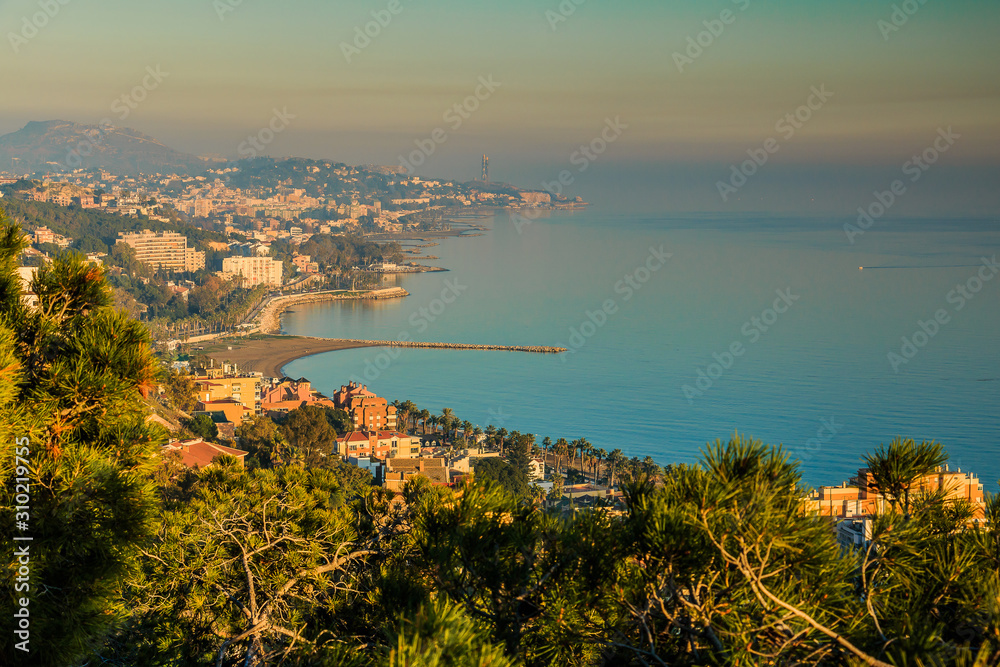 View of the Spanish Mediterranean coast in Nerja from the Balcon de Europa. Sunny autumn day with a view of a village and hills on the horizon. Blue sky with clouds and palm trees in the foreground