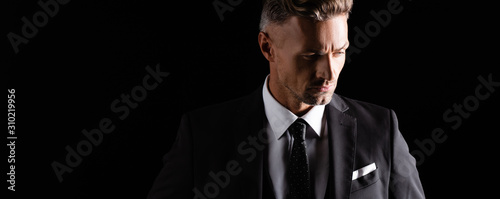 Panoramic shot of handsome businessman looking away isolated on black