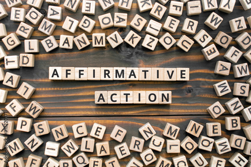 affirmative action- phrase words from wooden blocks with letters, affirmative action  support members of a disadvantaged group concept, random letters around, wooden background
