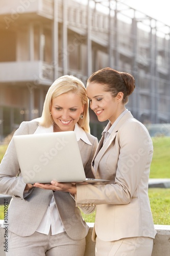 Happy young businesswomen using laptop together against building © moodboard