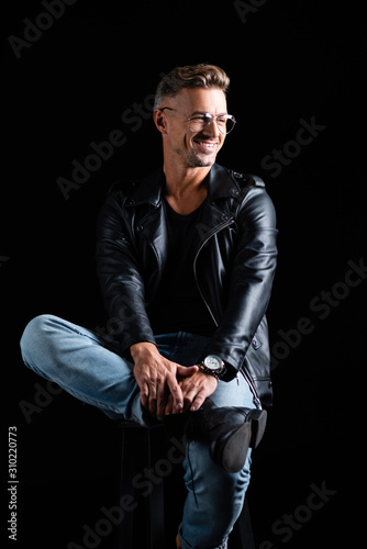 Smiling stylish man sitting on chair isolated on black