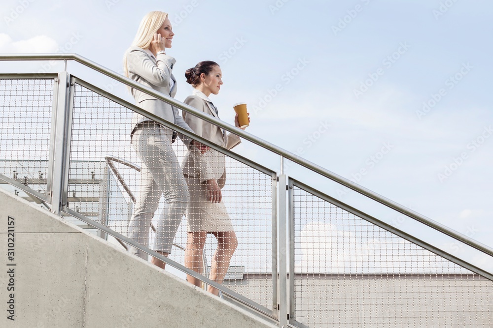 Profile shot of businesswomen moving down stairs against sky