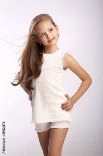  young beautiful blonde with wavy hair in a white summer dress smiling and posing in the studio for the camera on a gray background with blue eyes with a confident look