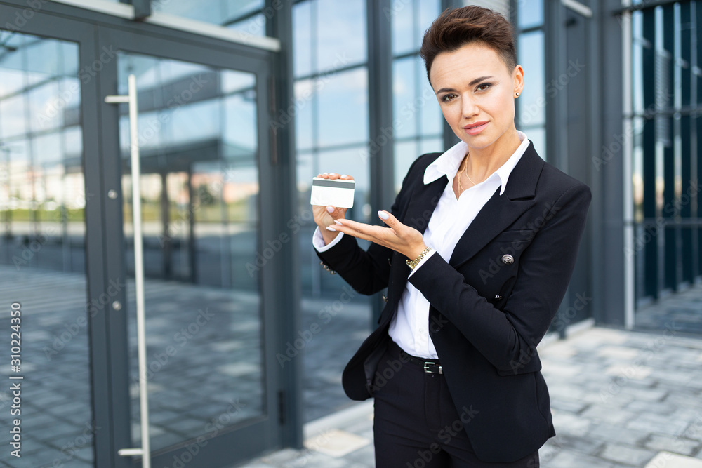 Caucasian woman in office clothes holds a credit card and waits colleague near the office building