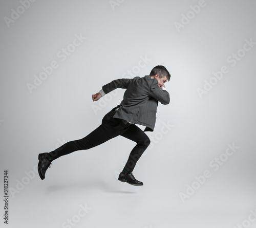 Hurry up, you're wild and young. Caucasian man in office clothes running like a professional sportsman on grey background. Businessman training in motion, action. Sport, healthy lifestyle concept.