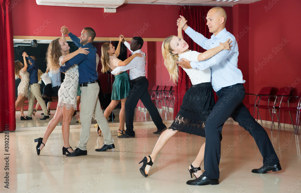 Positive adult couples dancing tango together  in modern studio