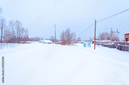 winter village in the snow on a sunny day. street of wooden houses road at houses near the forest, no people. 