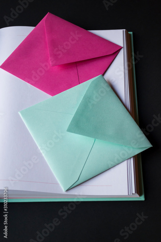 The turquoise and pink colors envelopes on the opened notepad, close up. 