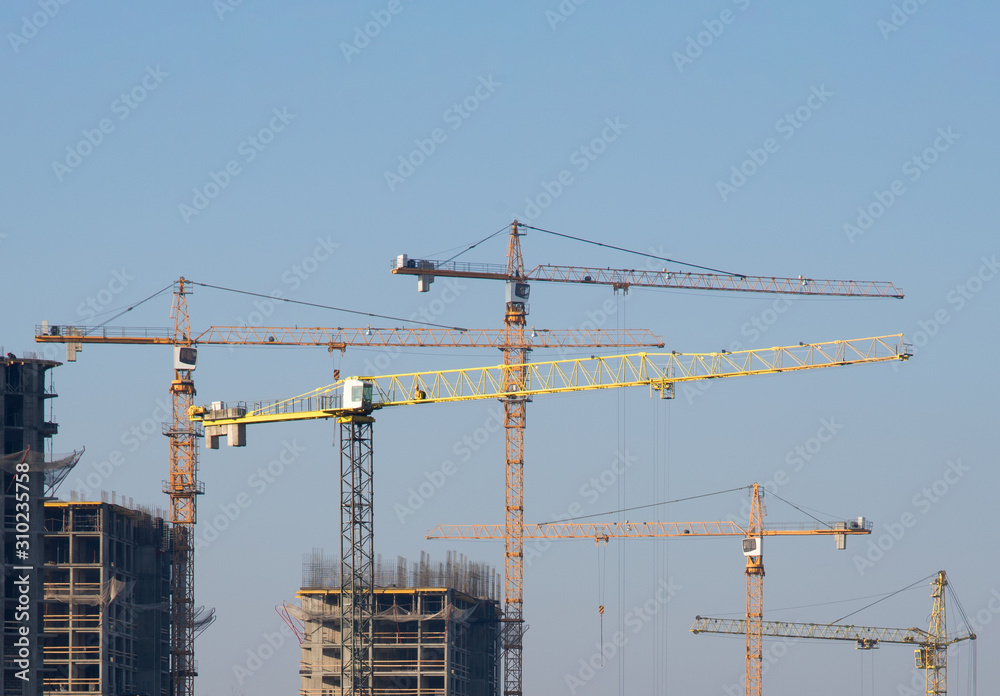 Tower cranes constructing a new residential building at a construction site against blue sky. Renovation program, development, concept of the buildings industry.