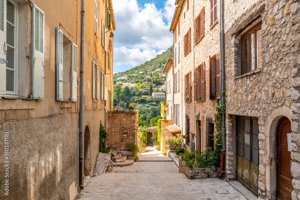 The Alpes-Maritimes mountains and towns of Southern France are visible from a medieval street in Tourrettes Sur Loup, France, on the French Riviera