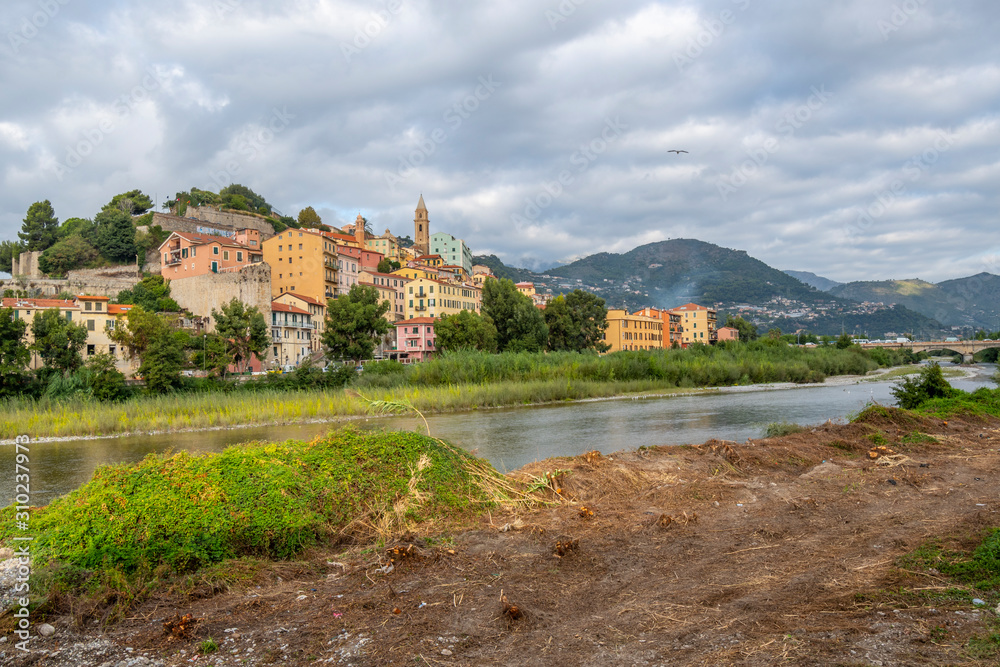 View from a riverbank across the river Roya of the village of Ventimiglia, Italy, and inland to the mountains of the Imperia region. View from a riverbank across the river Roya of the village of Ventimiglia, Italy, and inland to the mountains of the Imperia region.