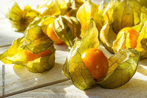 Many yellow ripe physalis fruits (Physalis peruviana) in the sunshine on a white wooden table. Fruits and vegetables, vegetarian and healthy eating. Ready to eat. photo