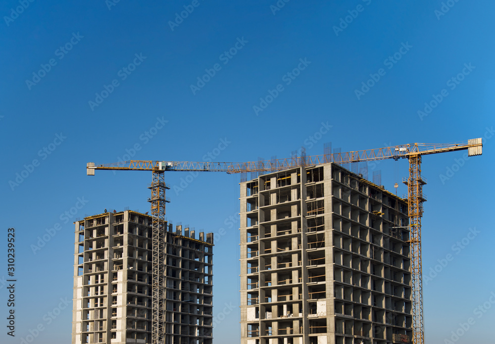 Tower cranes constructing a new residential building at a construction site against blue sky. Renovation program, development, concept of the buildings industry.