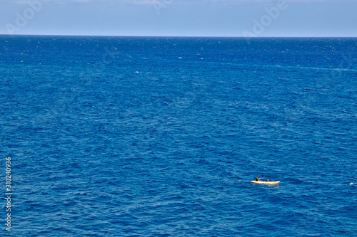 Yellow boat with two unidentified people in the ocean and the horizon showing on top