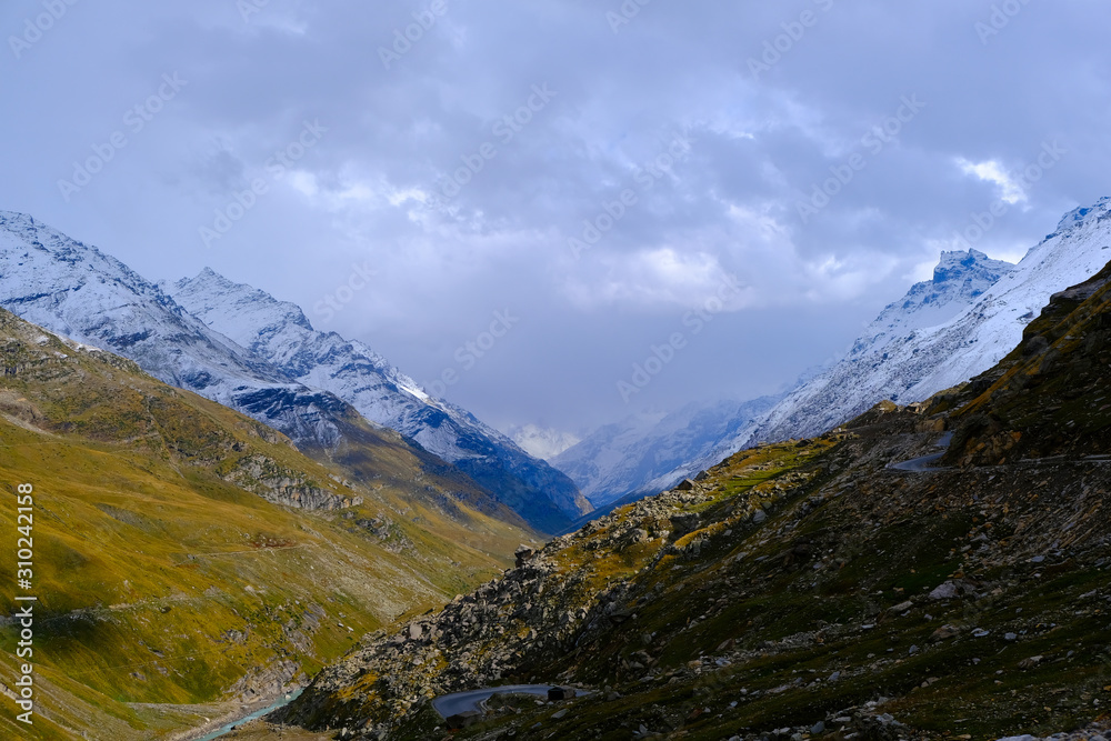 Fototapeta premium Beautiful view of the mountains covered with greenery and snow-capped peaks between which the river flows and winds the road. 