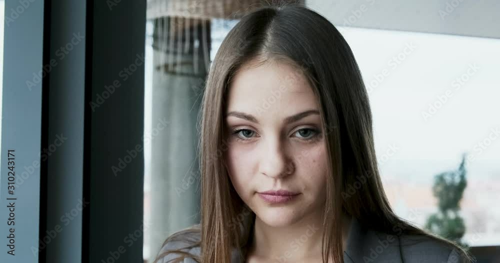 Portrait of young attractive female who looking at the camera on the office near window. Cheerfully pretty woman. Close up Portrait of young attractive female who looking at the camera on the office near window. Cheerfully pretty woman. Close up