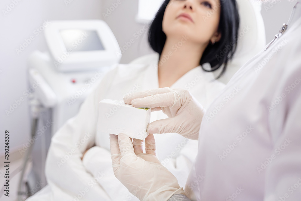 Hands of cosmetologist are holding new preparation for skin firmness and elasticity on blurred female client background. Concept of beauty and youth from new innovative cosmetic product. Copyspace Hands of cosmetologist are holding new preparation for skin firmness and elasticity on blurred female client background. Concept of beauty and youth from new innovative cosmetic product. Copyspace