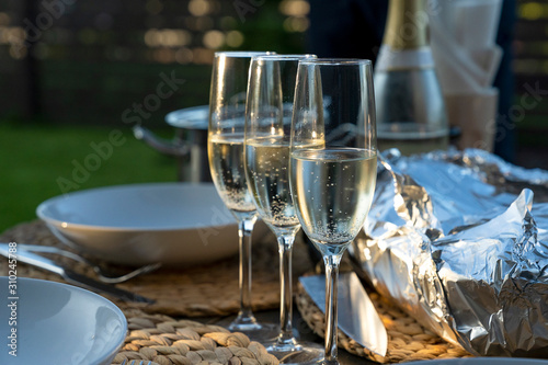 Sparkling white wine glasses and foil wrapped barbecue on a table. Dinner party at homes  terrace.