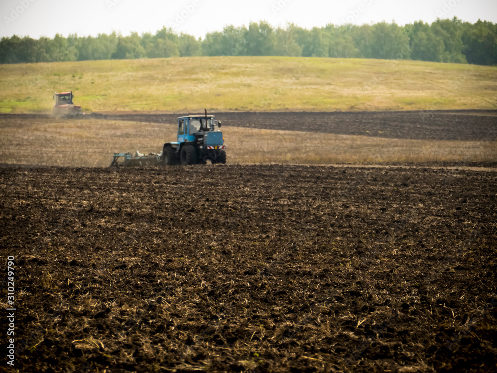 Fototapeta premium Tractors plow plowland on an autumn clear day