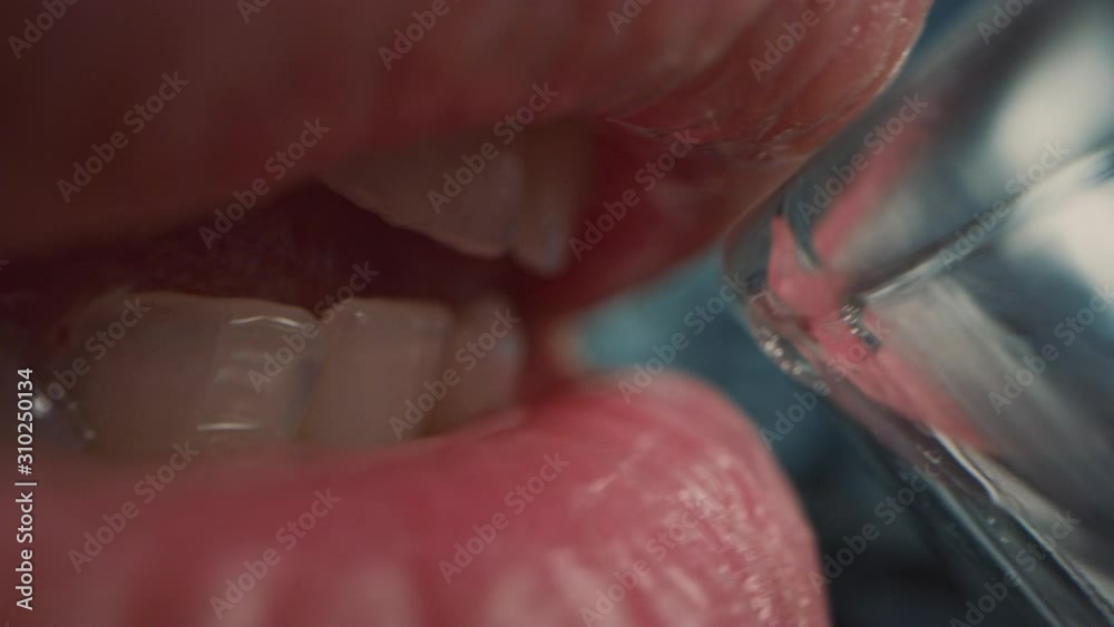 Extreme Close Up Macro Shot of a Person Drinking Water from a Transparent Glass. Fresh Tap Water Flows Inside the Mouth. Natural Mouth with Perfect White Teeth and Red Lips.