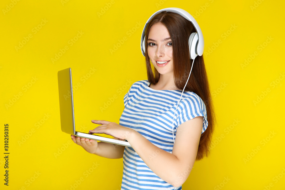 Young woman in headphones using laptop computer on yellow background Young woman in headphones using laptop computer on yellow background