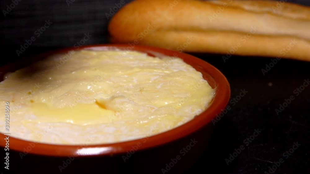 Baguette is dipped in preheated soft Saint-Felicien cheese in small ceramic pot Baguette is dipped in preheated soft Saint-Felicien cheese in small ceramic pot