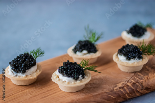 Tartlets with black caviar on wooden board.