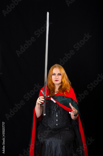 red-haired witch wearing in a long black gown and green robe controls fly of magic sword photo