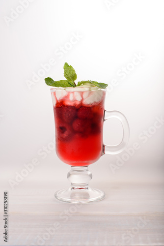 One glass glass with a cold raspberry drink with whipped cream and mint on top on a light background.